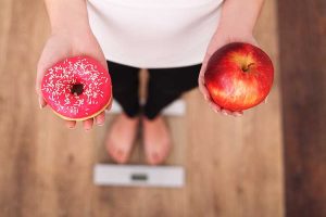 Diet. Woman Measuring Body Weight On Weighing Scale Holding Donut and apple. Sweets Are Unhealthy Junk Food. Dieting, Healthy Eating, Lifestyle. Weight Loss. Obesity. Top View